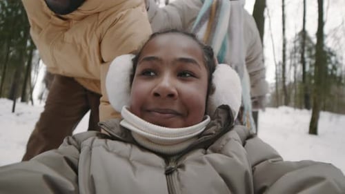 Smiling Girl Riding on Snow Sled in Winter Forest, Dad Pushing Her