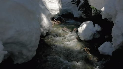 Flying Drone Over Flowing Stream In Snowy Ice Cave Tunnel