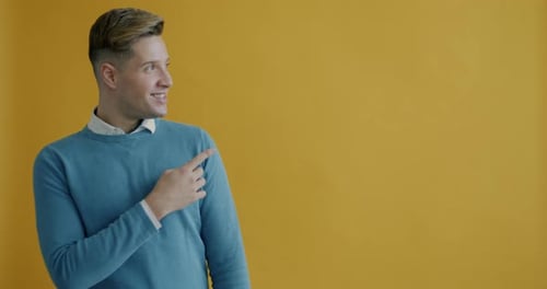 Portrait of Cheerful Young Man Pointing Sidewards Smiling Recommending and Attracting Attention