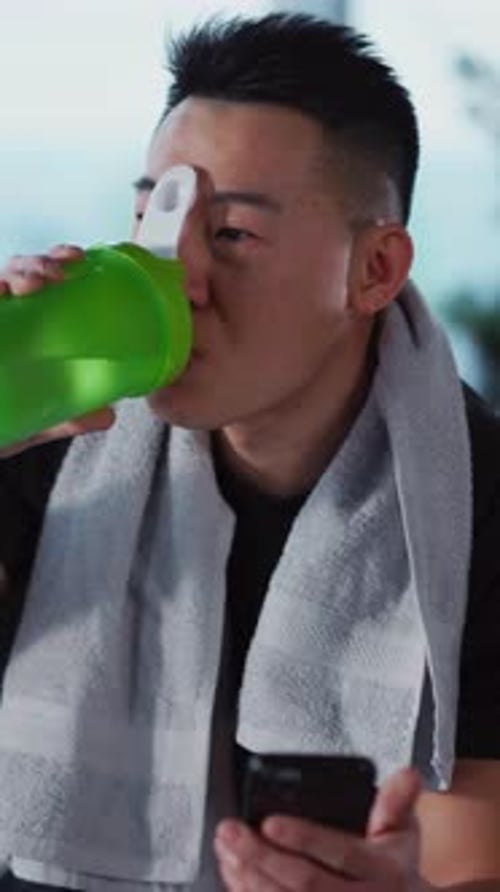 Man Drinks from Bottle While Using Phone Indoors