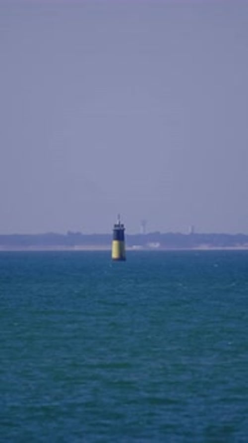A lighthouse in the middle of the sea, with an island behind it, ocean, water