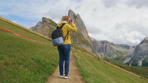 Une femme blonde avec un sac à dos prend des photos de la magnifique montagne de Seceda