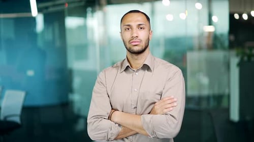 Portrait a young adult man in shirt looking seriously at camera in a modern office. Confident employ