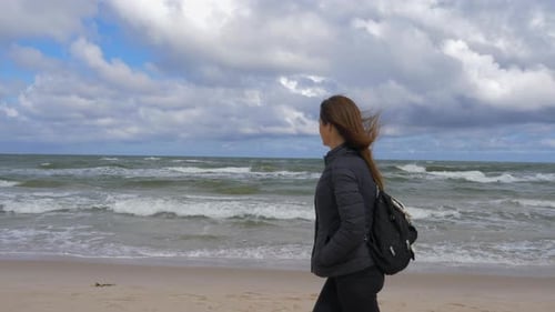 Shot of woman walking along the beach shore and looking melancholy at the beauty of the natural land
