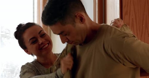 Woman Helps Man Into Military Uniform
