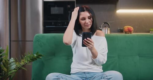 Female holding phone texting message technology app, typing email at home. Woman sitting on a green