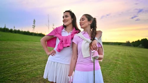 Two women dressed in white and pink clothes talking on the golf course