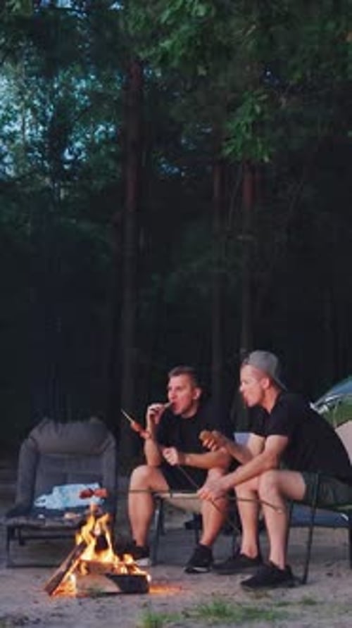 Two Men Relaxing by a Campfire in the Forest at Night