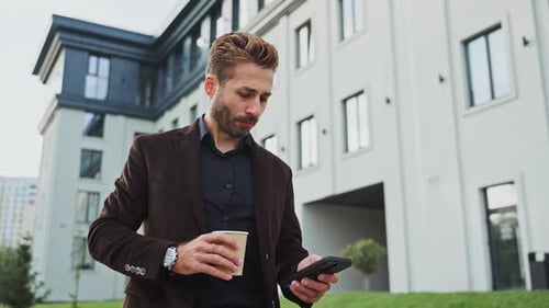 Young Man Checks Phone While Enjoying Coffee Outside Modern Apartment Building