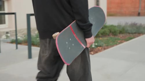 Skateboarder Holding Worn Skateboard Walks at Street