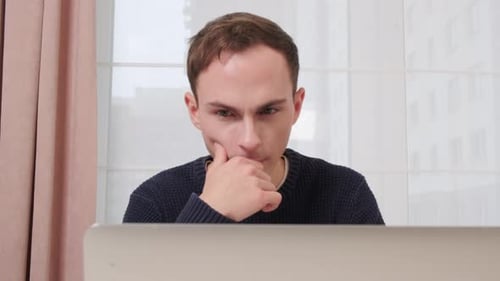 Young Man Sitting at a Desk in the Office and Working with a Laptop