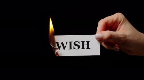 Woman Hand Holding Flamed Paper with Word Wish in Studio
