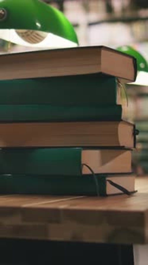 Vertical Video Close Up Green Books in Piles Placed on Table Desk in Library Under Green Lamps