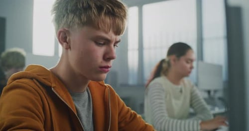 Male Student in Orange Hoodie Works on Computer Writing Code for Game Development Project
