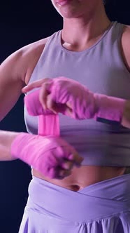 Zeitlupenkämpferin wickelt ihre Hände mit rosa Boxbandagen ein Boxtraining in einem dunklen Fitnessstudio