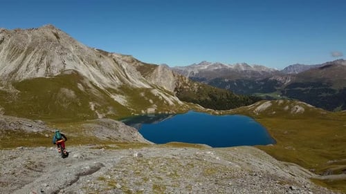 biker with colorful clothes goes down the path to the Rims Lake, aerial steady shot
