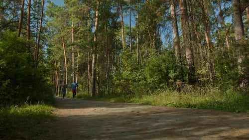 Young Man and Woman Jogging Together Down Narrow Path in Forest