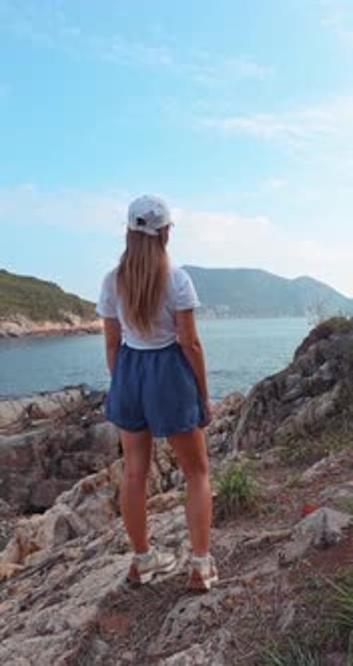 Woman Standing on Rocky Cliff Overlooking Ocean Bay