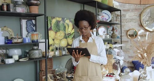 Smiling african american woman working on tablet in own shop and looking at camera. Small business