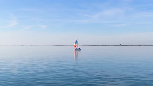 Drohnenaufnahme einer einzelnen Segelyacht in ruhiger See mit leichtem Wind.