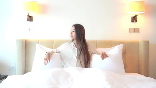 Une jeune femme assise dans un immense lit confortable se penche sur un énorme oreiller confortable. Titre spa