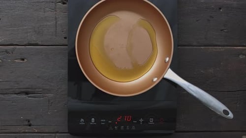 Woman's hands preparing frying oil on induction stove top in kitchen time lapse