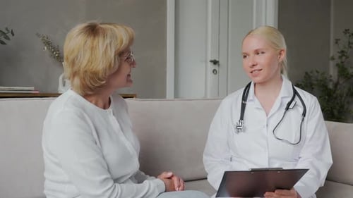 A Young Woman Doctor Communicates with an Elderly Woman in a Home Interior