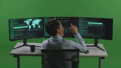 Back View Of Asian Man Thinking While Write Code With Multiple Computer Screens In Green Screen