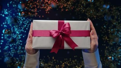 Silver Wrapped Gift held in Front of Bokeh Lights