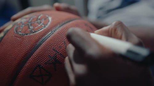 Hands of Sportsman Making a Sign on Basketball with Marker