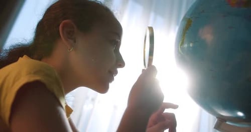 Girl Exploring World Globe with Magnifying Glass at Home