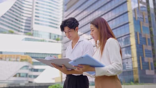 Asian young businessman and woman partner working outdoors in the city.