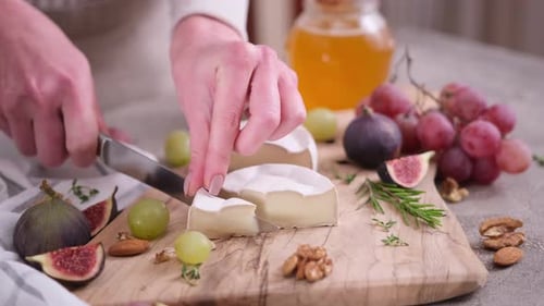 Woman Slicing Camembert or Brie Cheese on Wooden Cutting Board at Domestic Kitchen