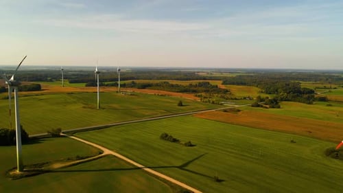 Drone shot of the wind turbines working in a wind farm generating green electric energy on a wide gr