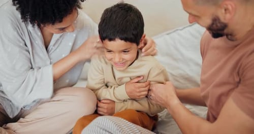 Family Time: Parents Tickle Smiling Boy on Bed