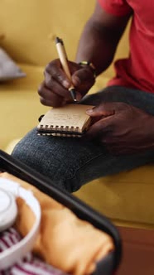 Person Writing Packing List Beside Open Suitcase