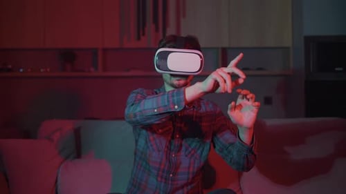 Young man at home in virtual reality glasses plays, works, studies. Man with VR glasses