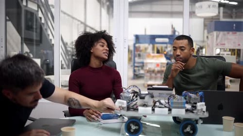 Multiracial team of engineers testing a robotics prototype in modern factory, discussing and collabo