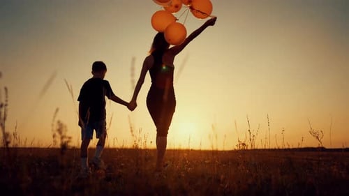 Happy Mother and Little Son Holding Hands and Walking in Field Balloons in Hand Calm Scenery in