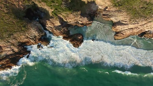 Cinematic Aerial View of White Foam Crashing Against Rocky Cliffs