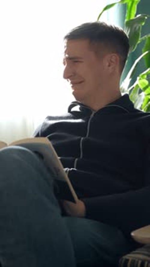 Vertical of Sad Man Reading Book in Cozy Apartment