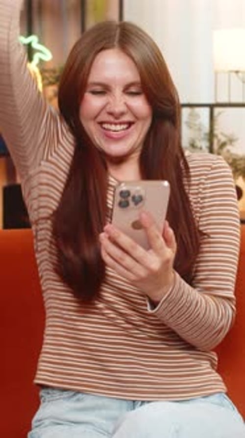 Enthusiastic woman celebrates success using smartphone indoors