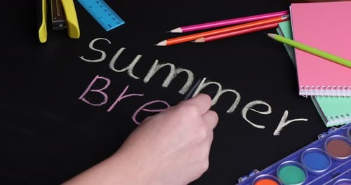 Woman writing phrase Summer vacation on chalkboard with school supplies, closeup