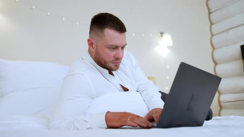 Man works on laptop while lying in bed
