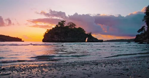 Indian ocean tropical beach with small rocky island at colorful sunset. Yellow dramatic cloudy sky.