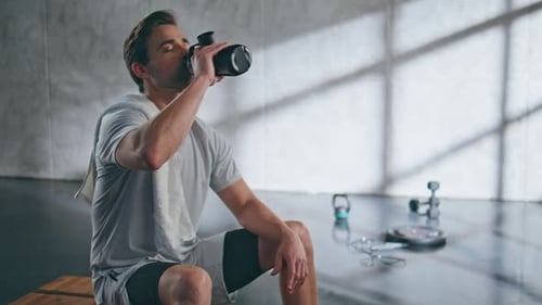 Exhausted Man Drinking Water From Sports Bottle After Fitness Training in Gym
