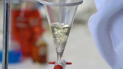 Science chemistry lab test, close-up as a lab tech pours liquid into a funnel.