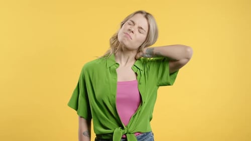 Woman Rubbing Stiff Neck Against Yellow Background