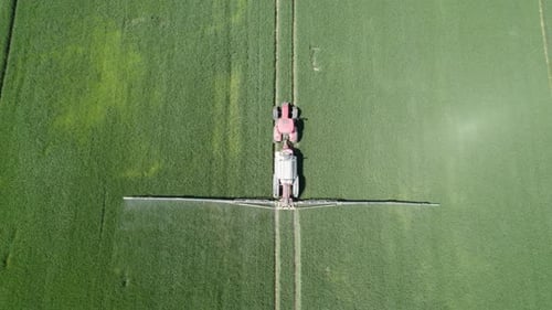 Aerial top-down shot of the agricultural sprayer spraying insecticide to the green field agricultura