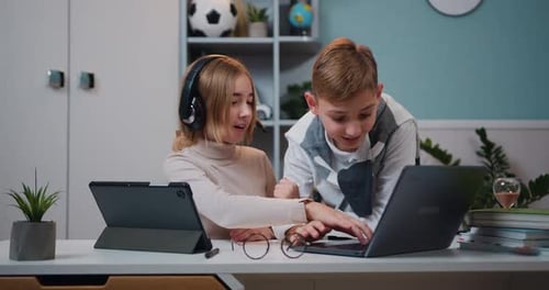 Pequeña y linda niña con auriculares usando juegos de Internet en una tableta digital mientras el niño juega